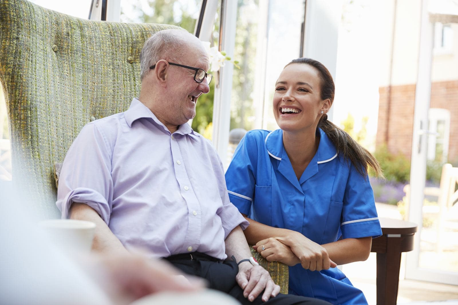 CHPNA Certification – Preparation and Resources Senior man laughing with an attentive caregiver at home in a hospice and palliative care setting as part of CHPNA exam preparation